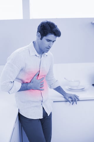 Casual young man with stomach pain standing in the kitchen at home