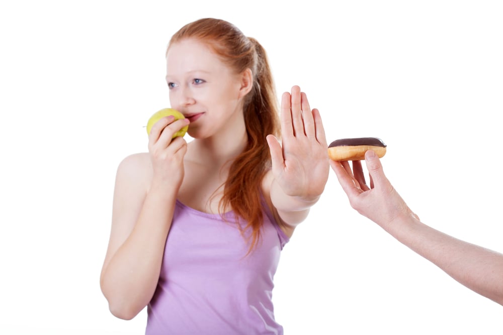 Girl with apple refusing cookie on isolated white background